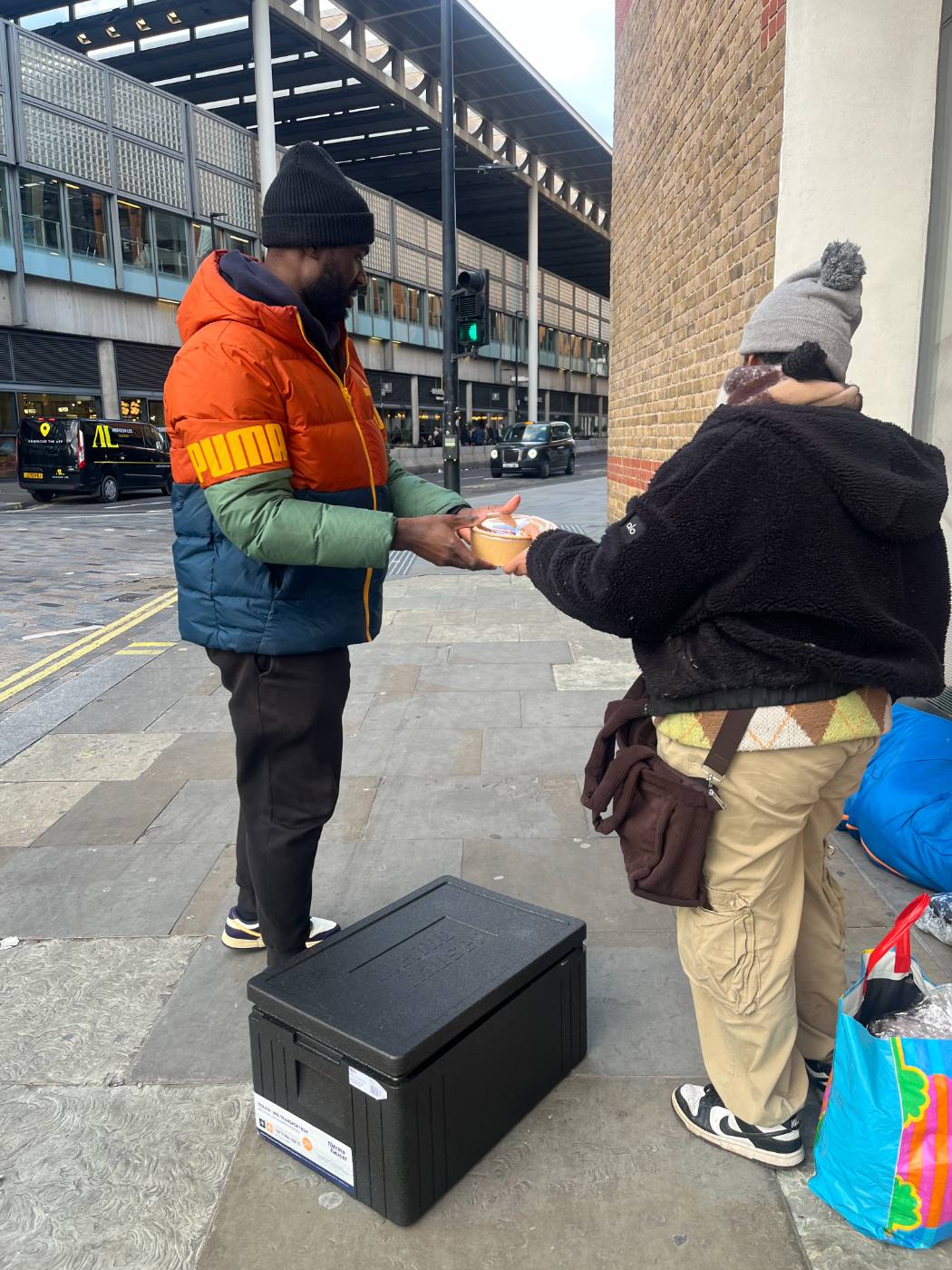 A volunteer handing a hot meal to someone on the street